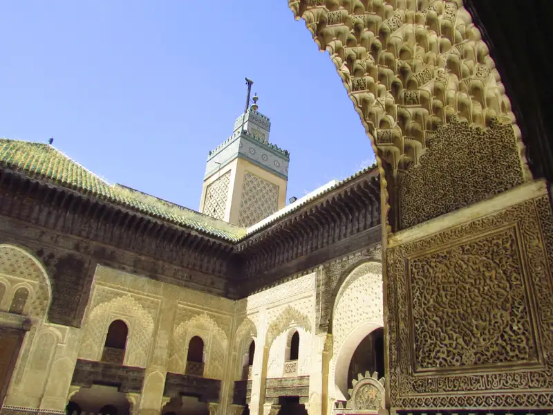 Architektur einer Medrese: Blick durch einen kunstvoll verzierten Bogen auf den Innenhof mit Minarett.