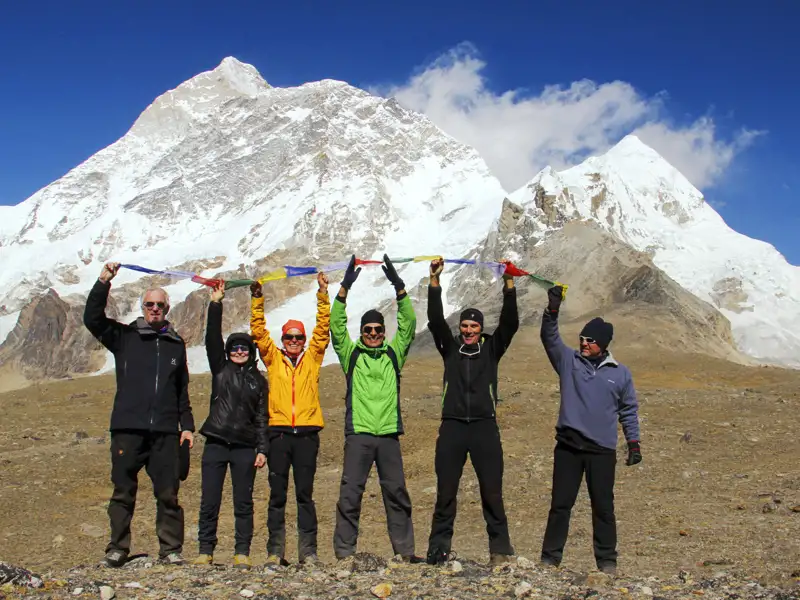 Wandergruppe feiert den erfolgreichen Aufstieg mit Gebetsfahnen vor dem Himalaya-Gebirge.