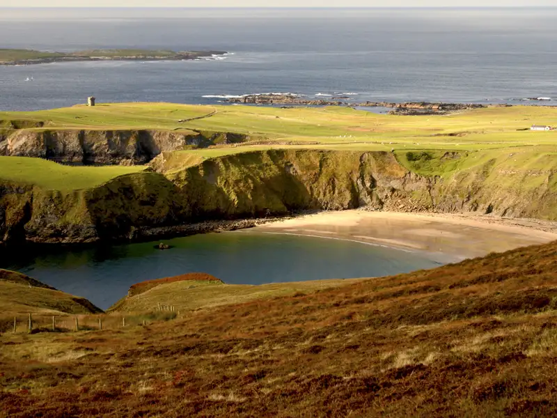 Abgeschiedene Bucht mit Sandstrand, grünen Hügeln, Klippen und altem Turm an der irischen Küste.