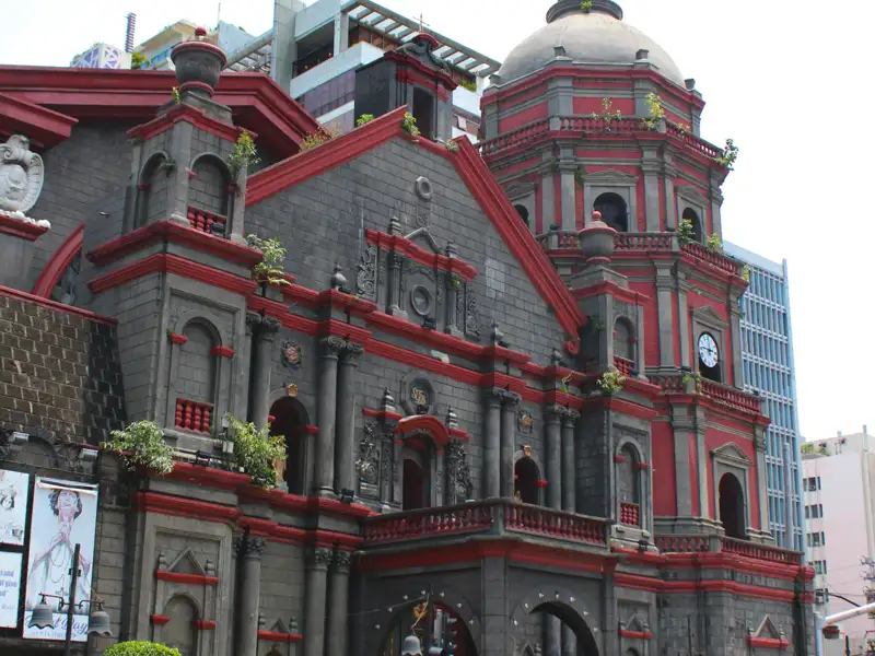 Historische Kirche mit grauer Steinfassade und roten Akzenten. Der Turm mit Kuppel ist ein markantes Merkmal.