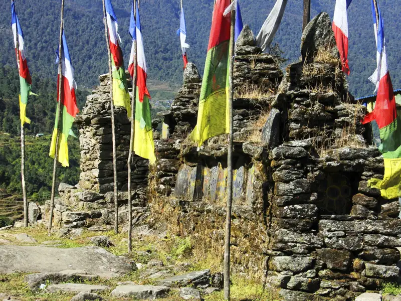 Gebetsfahnen an einer Steinmauer in der Berglandschaft.