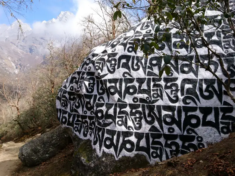 Bemalter Felsbrocken mit tibetischen Mantras auf einem Bergwanderweg.
