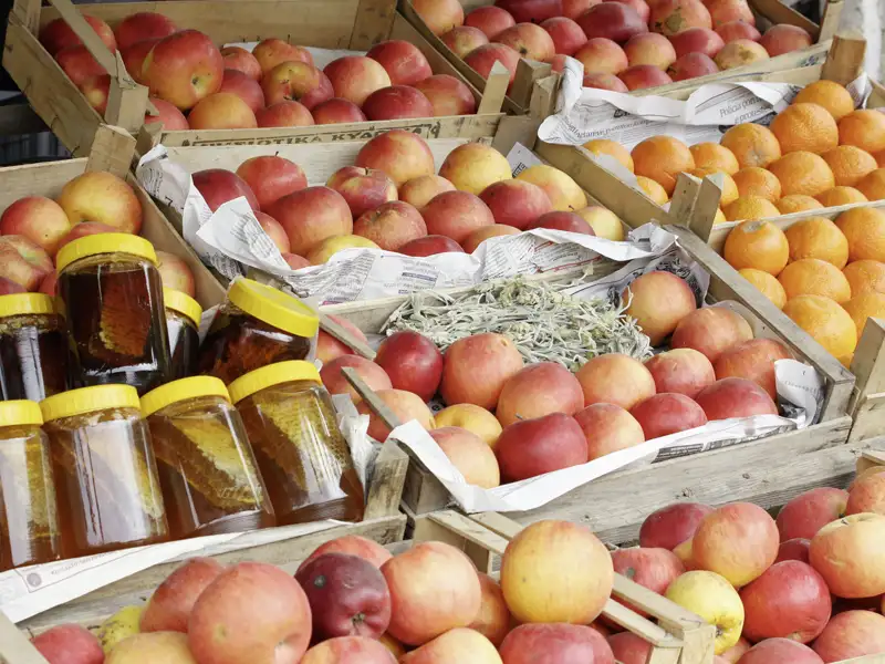 Auslage mit Äpfeln, Orangen und Honiggläsern auf einem Markt.