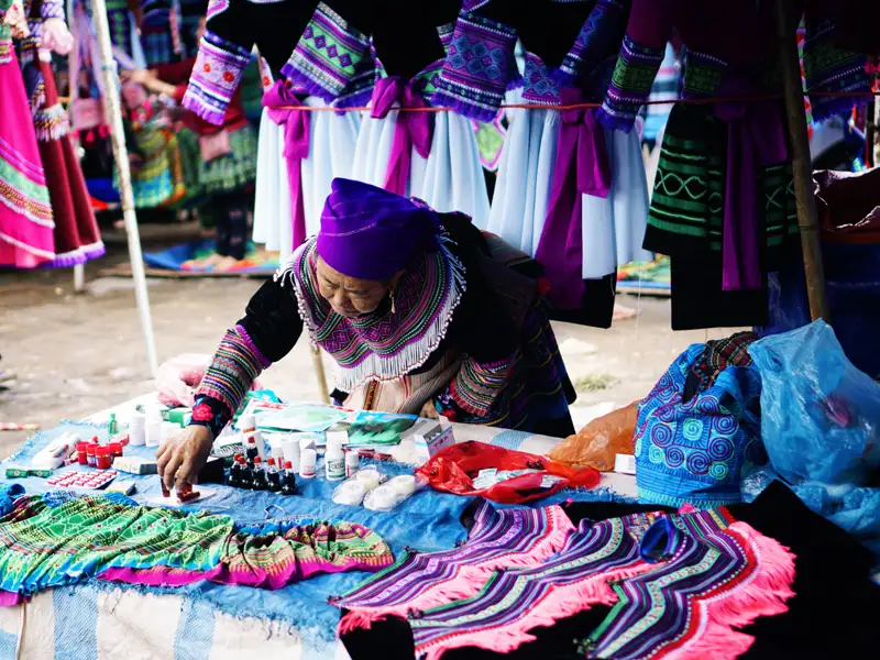 Marktverkäuferin in traditioneller Kleidung bietet handgefertigte Textilien und Waren an.