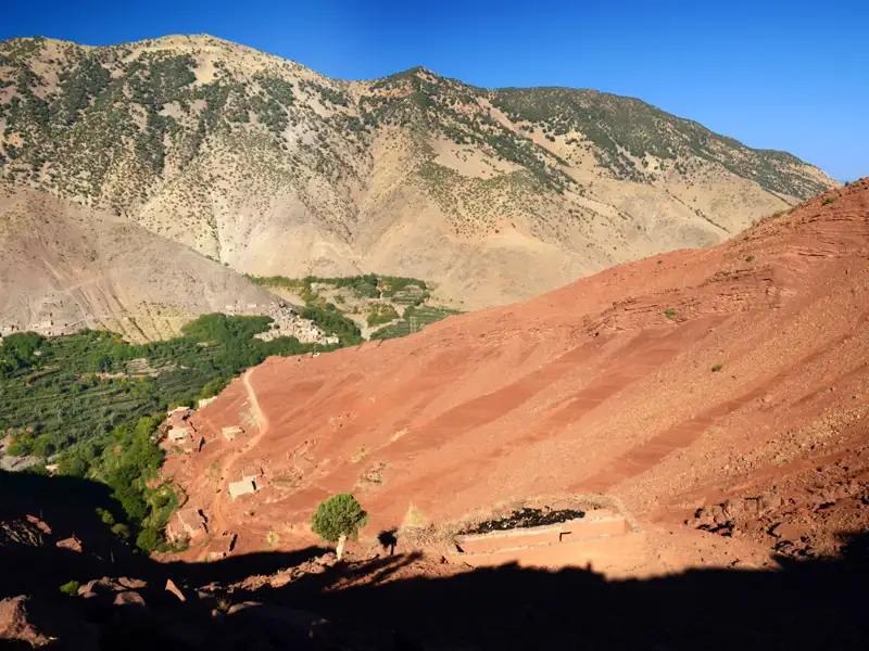 Kontrast zwischen roten Berghängen und grünem Tal in den Bergen.