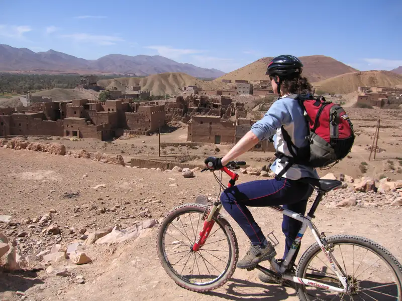 Mountainbikerin macht eine Pause auf ihrer Tour und blickt auf eine verlassene Siedlung in der Wüstenlandschaft.