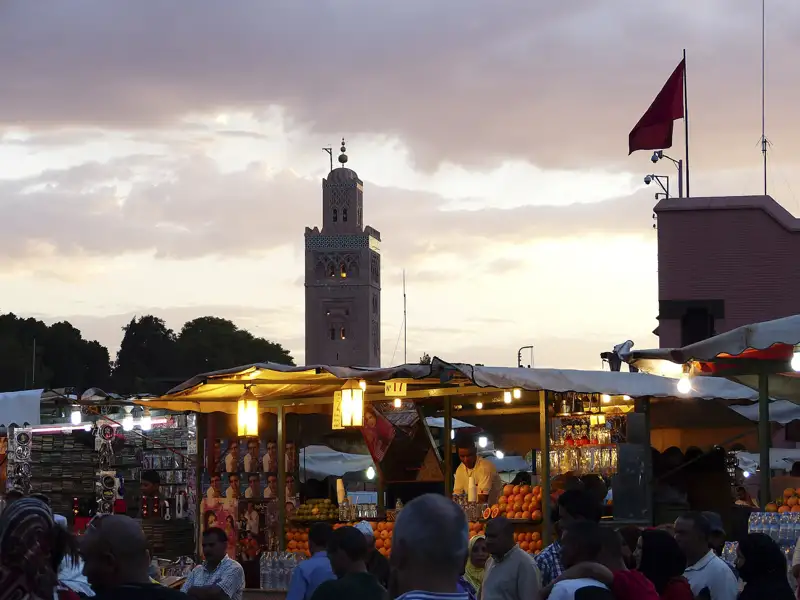 Marktstände mit Orangen und anderen Waren auf dem Djemaa el Fna in Marrakesch bei Sonnenuntergang. Die Koutoubia-Moschee ist im Hintergrund sichtbar.