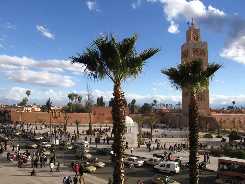 Platz in Marrakesch mit Minarett und Palmen.
