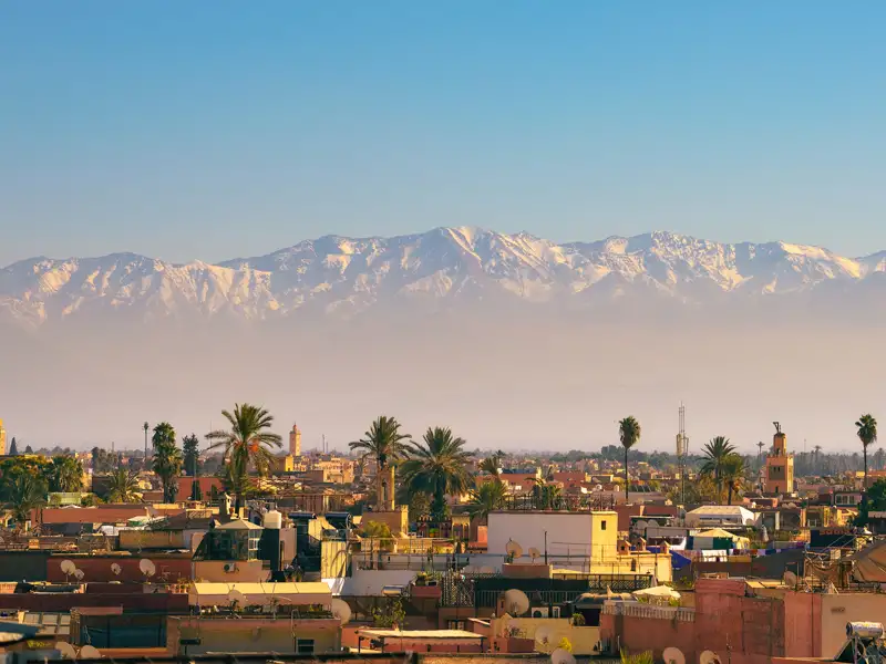 Blick auf die Dächer von Marrakesch mit dem schneebedeckten Atlasgebirge im Hintergrund.