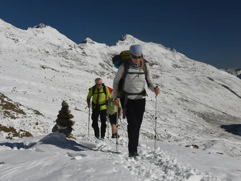 Wanderer auf einem verschneiten Bergpfad mit Wanderstöcken und Rucksäcken in den Bergen.