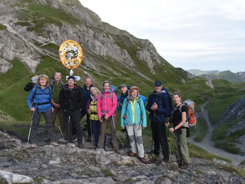 Wandergruppe am Wegweiser in den Bergen. Die Wanderer tragen Rucksäcke und Wanderstöcke.