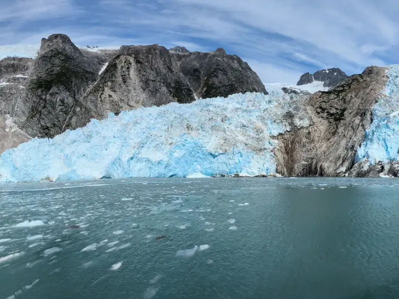 Kalbender Gletscher mit blauem Eis und umliegenden Bergen.