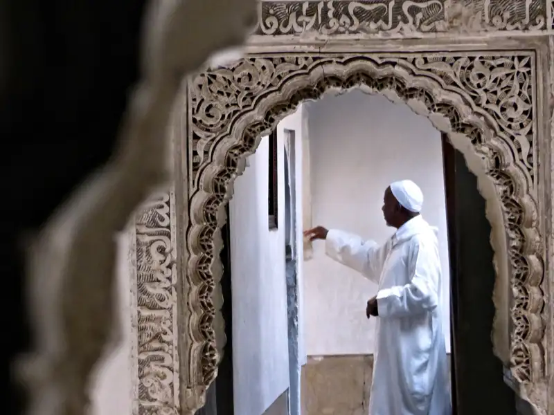 Mann in traditioneller Kleidung in einem verzierten Torbogen.