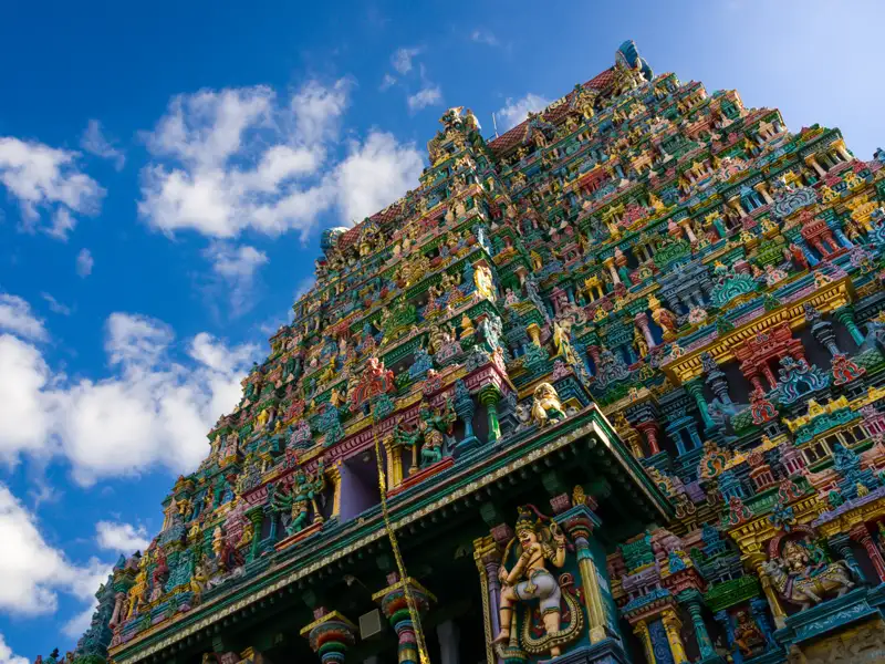 Bunter Tempel mit vielen Details und Figuren vor einem blauen Himmel mit Wolken.