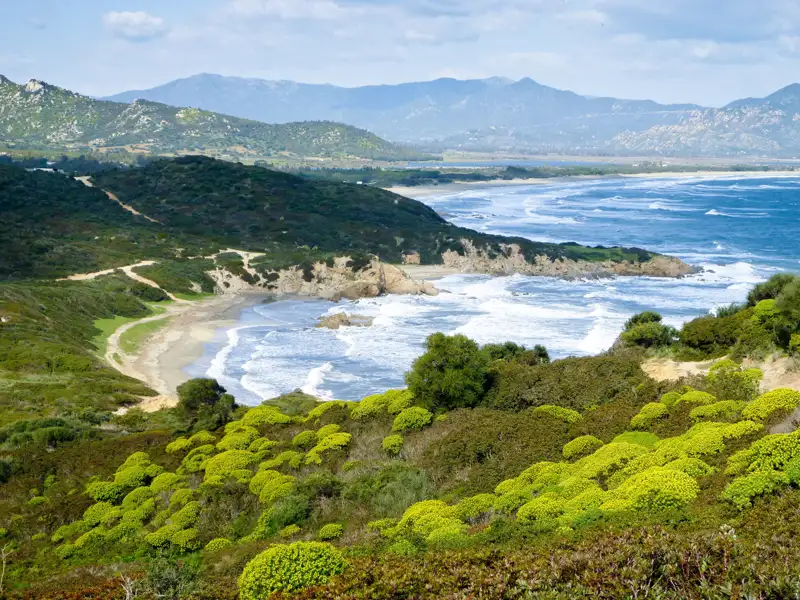 Sicht auf die Küste mit Strand und bewachsenen Hügeln.