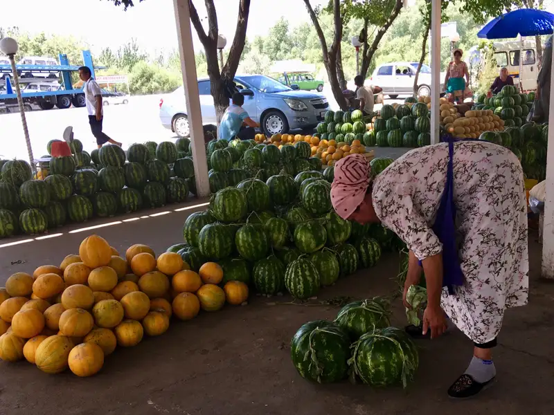 Marktstand mit Wassermelonen und Melonen. Eine Verkäuferin sortiert die Früchte.