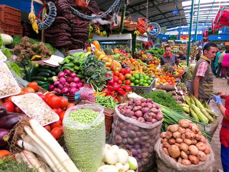Marktstand mit verschiedenen Obst- und Gemüsesorten wie Tomaten, Zwiebeln, Kartoffeln, Erbsen und Paprika.