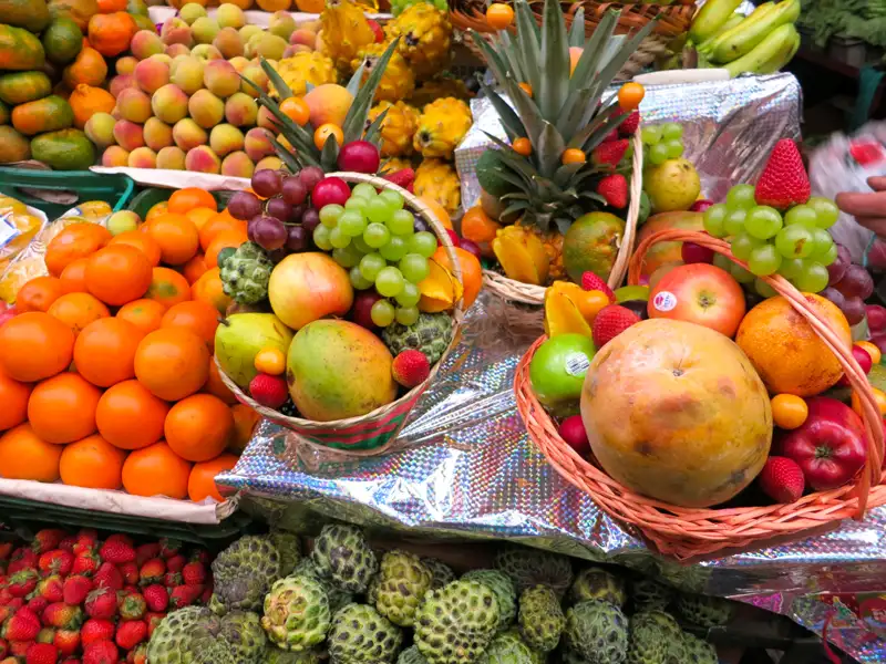 Auslage von verschiedenen Früchten auf einem Marktstand.  Körbe gefüllt mit einer bunten Mischung aus tropischen und regionalen Früchten.