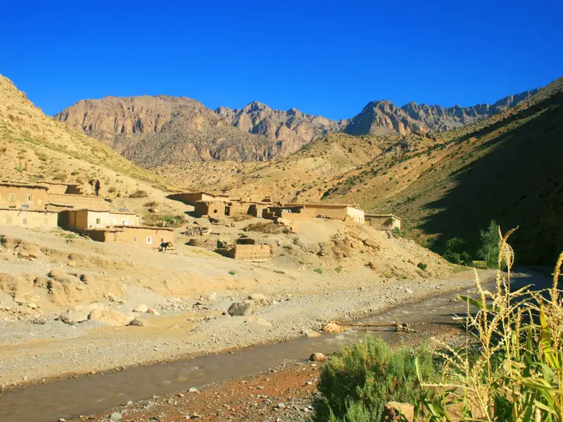 Traditionelles Bergdorf mit Lehmhäusern und einem Fluss im Vordergrund.