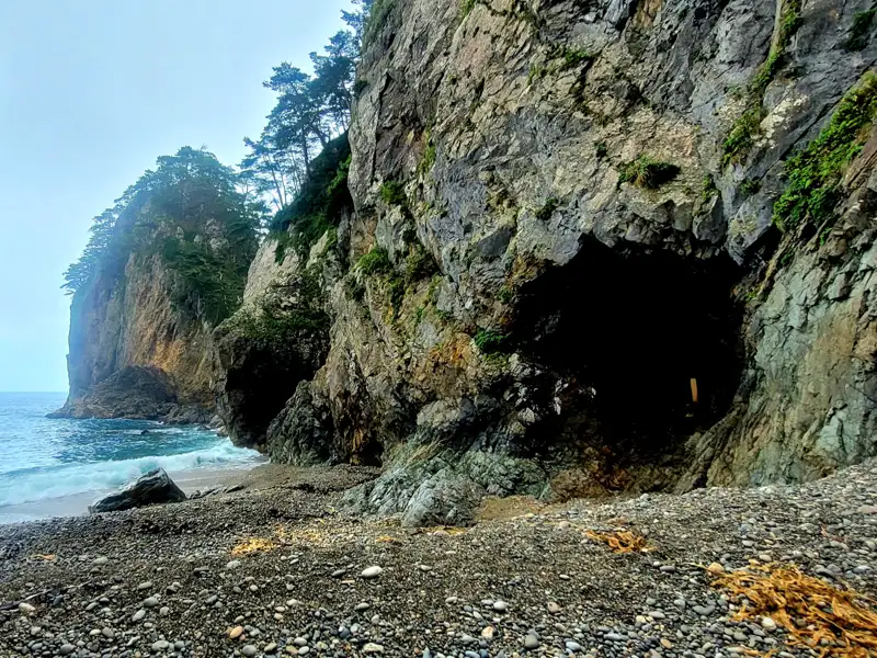 Felsige Küste mit einer Höhle und Kieselstrand.