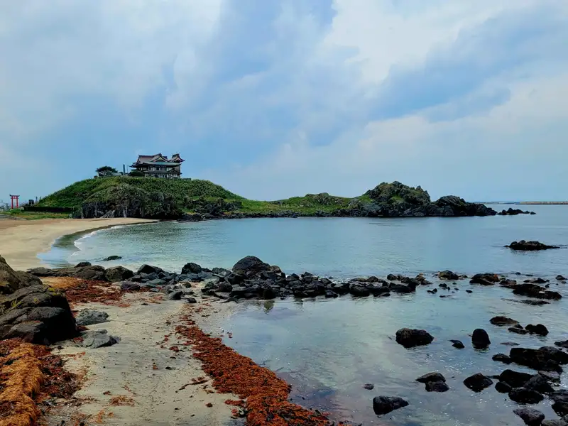 Traditionelles Gebäude auf einer Insel, felsiger Strand, bewölkter Himmel