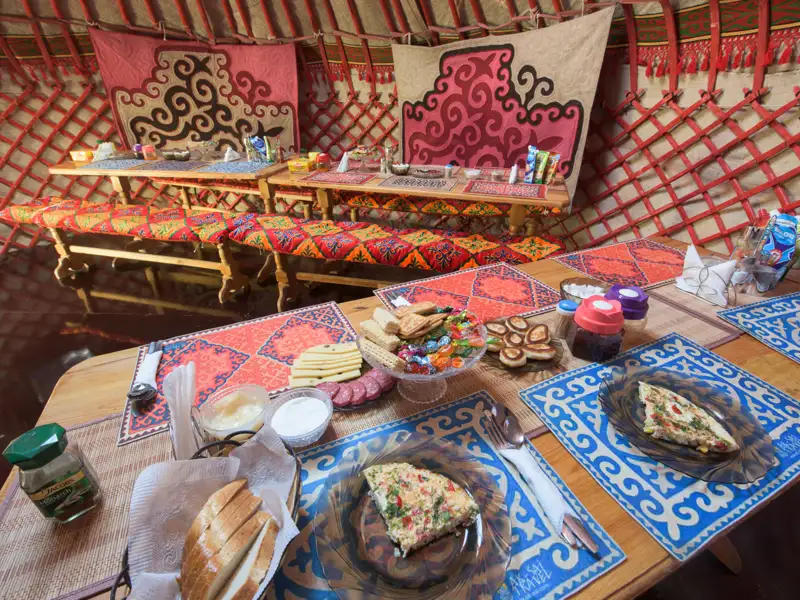 Traditionelles Frühstück in einer Jurte, serviert auf einem Tisch mit bunten Tischsets und landestypischen Speisen.