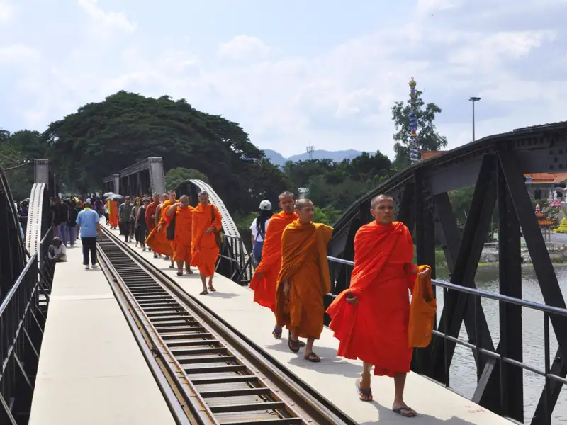 Mönche in orangefarbenen Gewändern gehen über eine Brücke mit Bahngleisen.