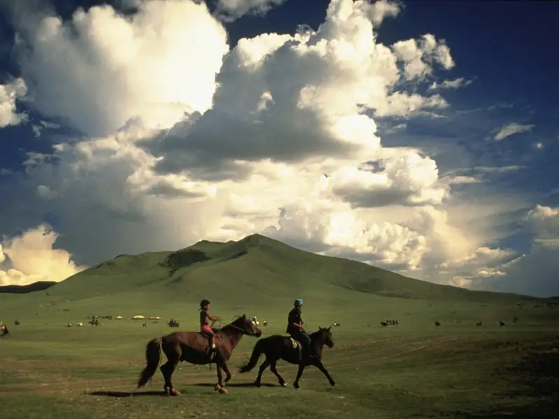 Zwei Reiter durchqueren eine weitläufige Landschaft mit sanften Hügeln unter einem beeindruckenden Himmel.