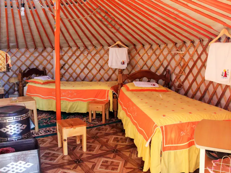 Blick in das Innere einer traditionellen Jurte, die zwei Betten, einen Ofen und Handtücher zum Trocknen bietet.