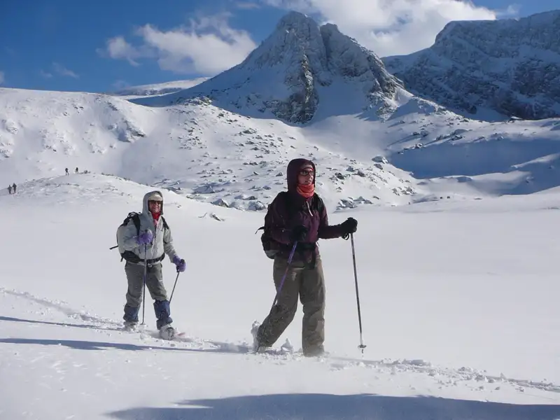 Zwei Schneeschuhwanderer durchqueren eine verschneite Berglandschaft.