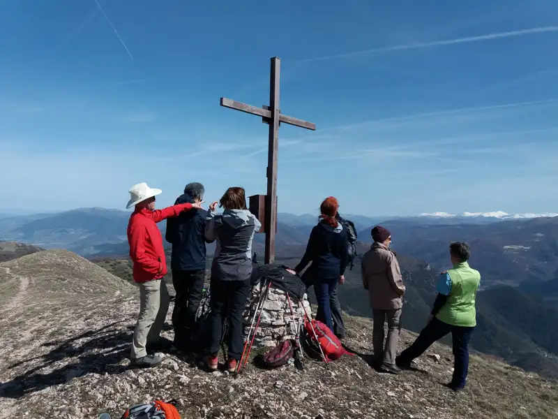 Wandergruppe am Gipfelkreuz mit Panoramablick auf die Berge.