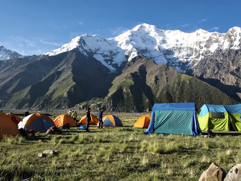 Campingplatz in den Bergen mit Zelten und schneebedeckten Gipfeln im Hintergrund.