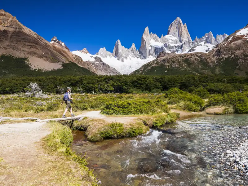 Wanderer überquert einen Bach in Patagonien mit dem Fitz Roy im Hintergrund.