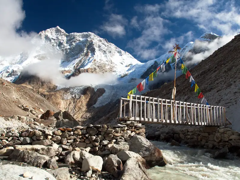 Holzbrücke mit Gebetsfahnen im Himalaya Gebirge.