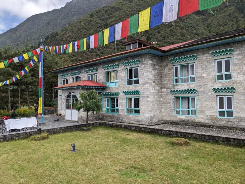 Gebetsfahnen wehen vor einem Steinhaus, das möglicherweise als Unterkunft während der Reise dient.
