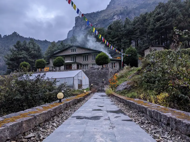 Weg zu einer Berghütte im Himalaya mit Gebetsfahnen und einem Gewächshaus.