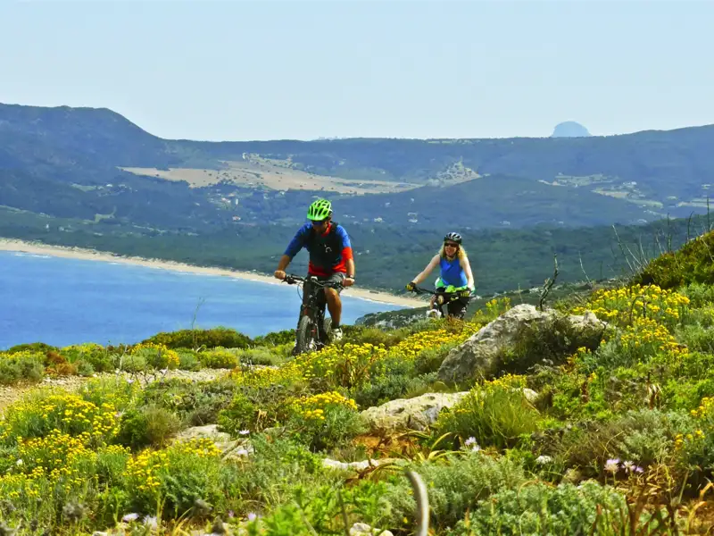 Mountainbiker auf einem Küstenpfad mit Blick auf das Meer und die Berge.