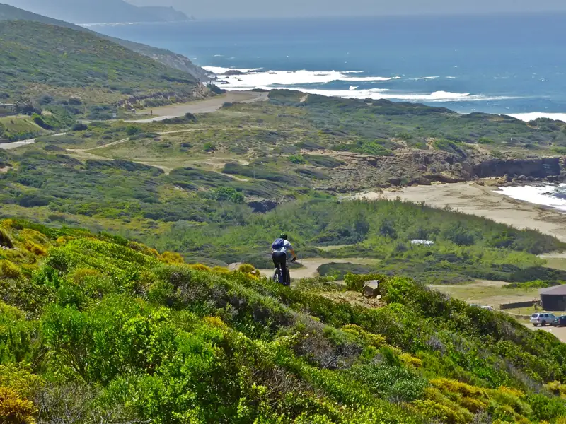 Mountainbiker auf einem Hügelweg mit Blick auf die Küste und das Meer.
