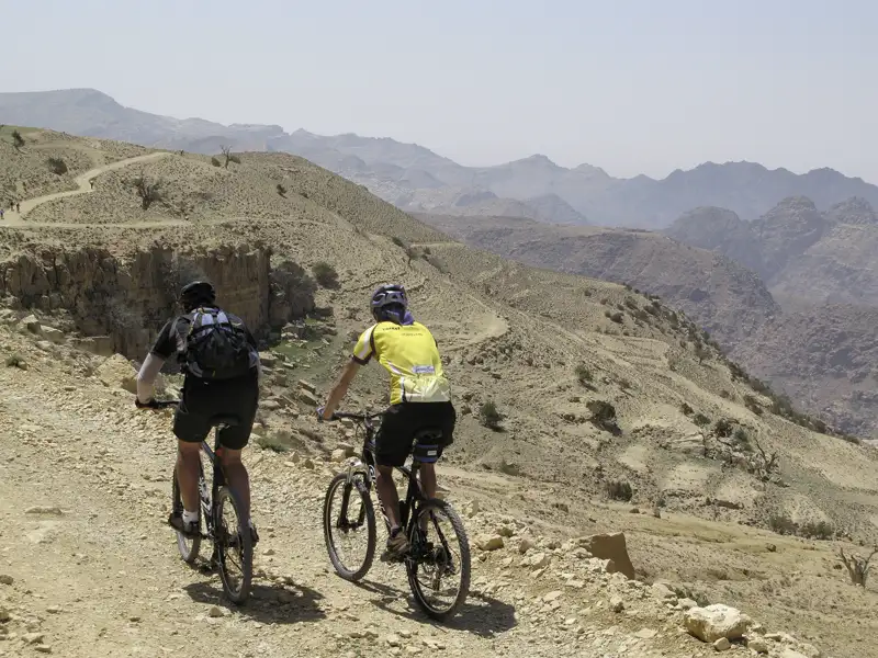 Zwei Mountainbiker auf einem Bergpfad in der Wüste.