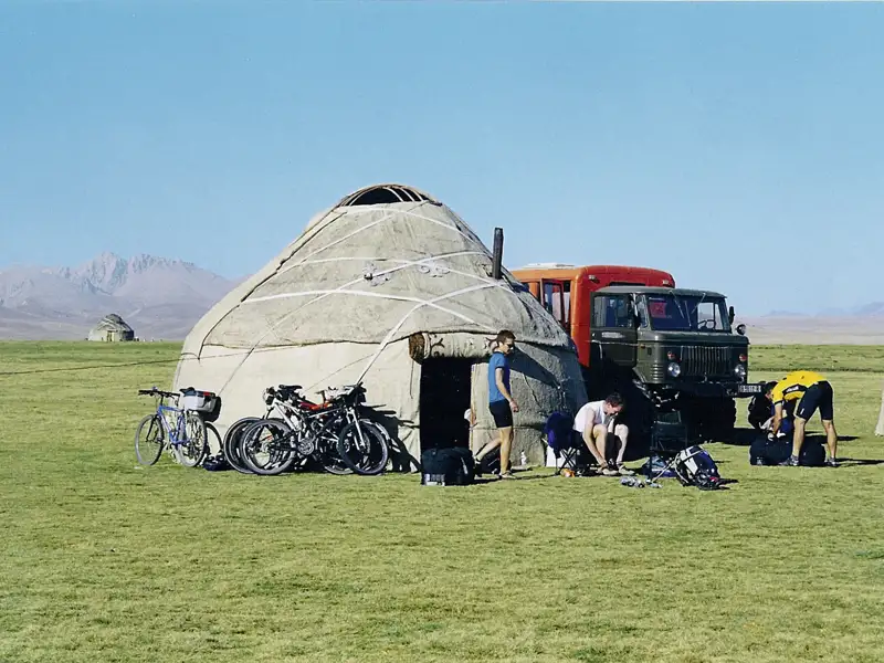 Reisende bereiten sich an einer Jurte mit Fahrrädern und einem Geländewagen auf die Weiterreise vor.