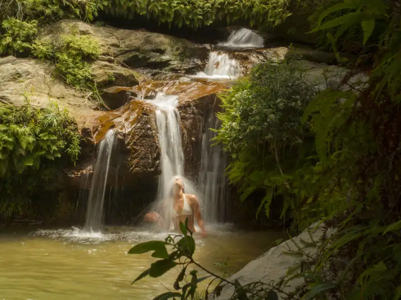 Frau unter einem Wasserfall im Dschungel.