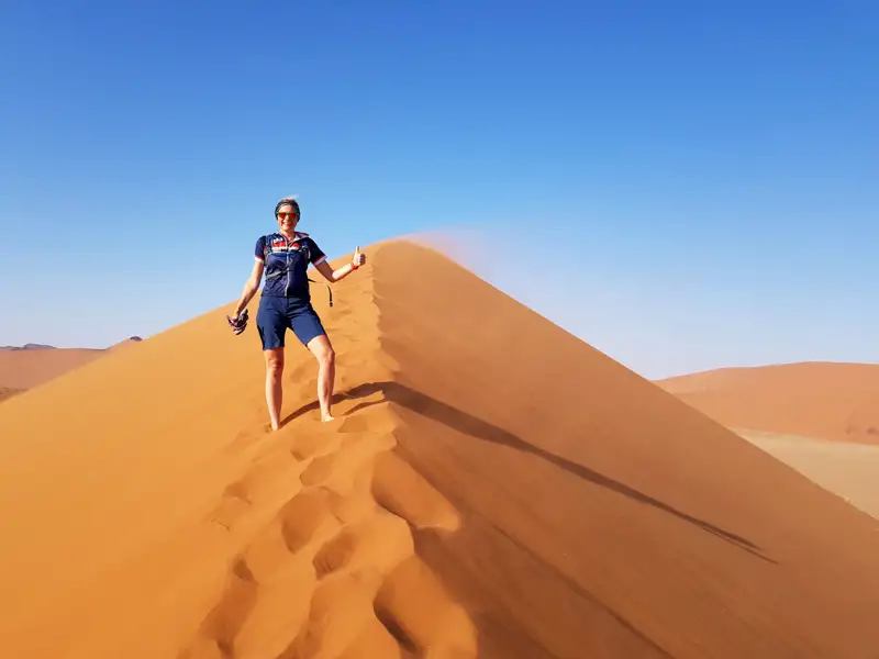 Eine Person steht oben auf einer Sanddüne und signalisiert Erfolg.