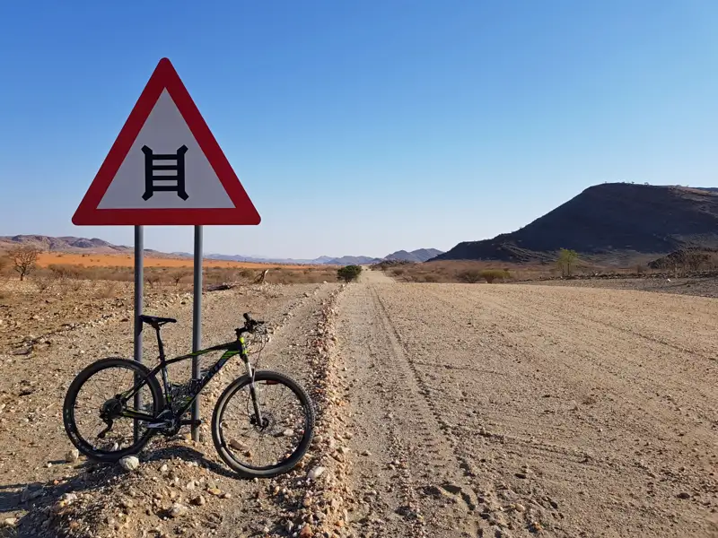 Fahrrad an einem Viehgitter-Warnschild auf einer Schotterpiste.