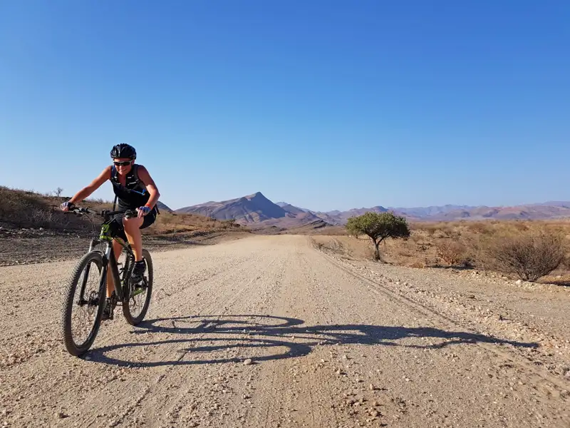Mountainbiker auf einer Schotterpiste in einer trockenen, bergigen Landschaft.