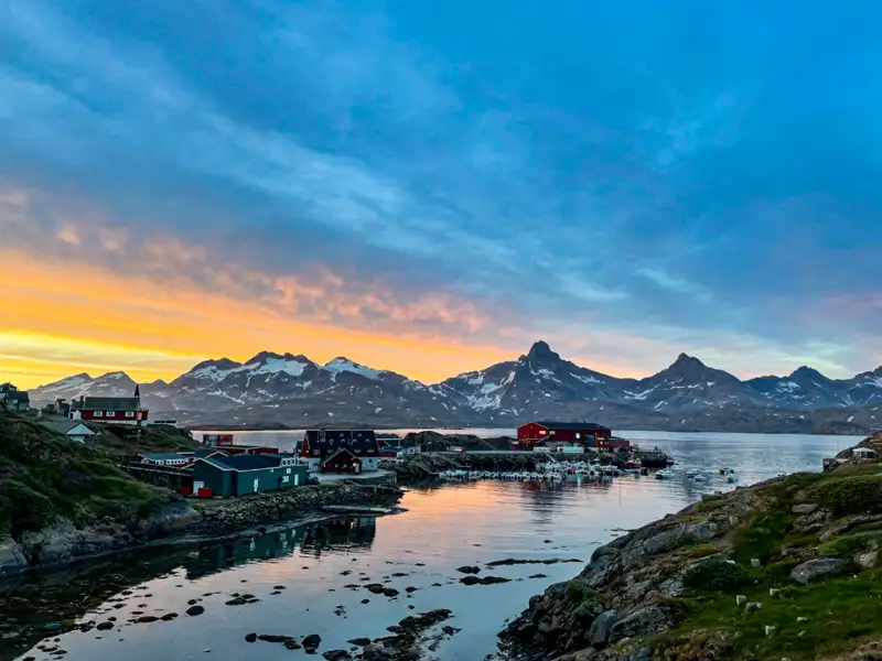 Sonnenuntergang über einem Küstenort und schneebedeckten Bergen in Grönland.