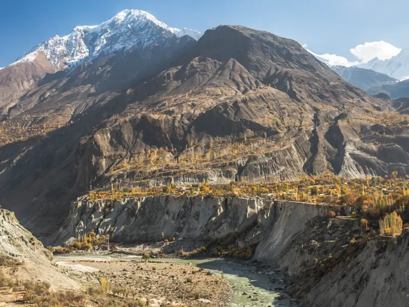 Blick auf ein Flusstal, umgeben von steilen Berghängen und schneebedeckten Gipfeln.