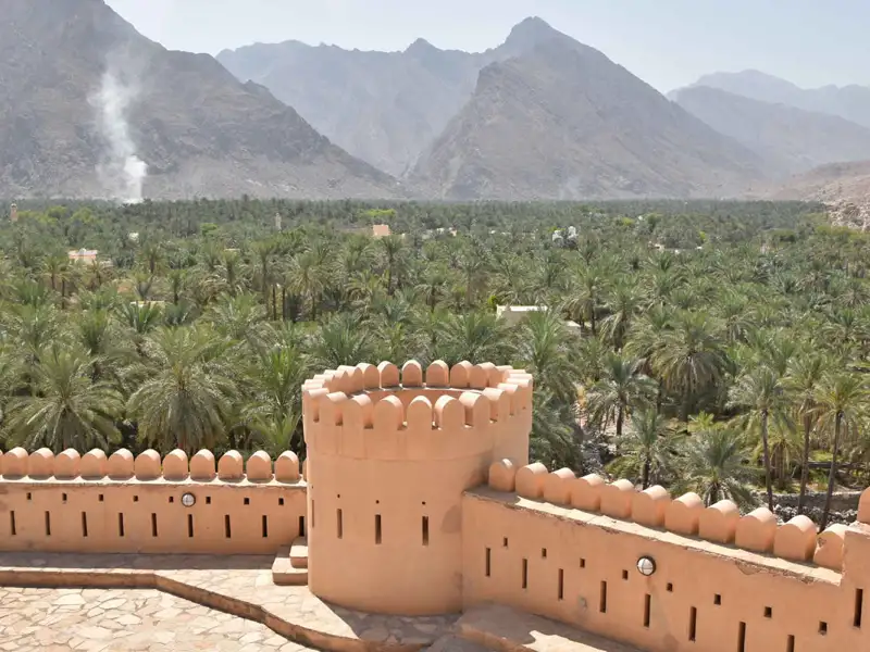 Blick von einer Festungsmauer auf eine Palmenoase mit Bergen im Hintergrund.