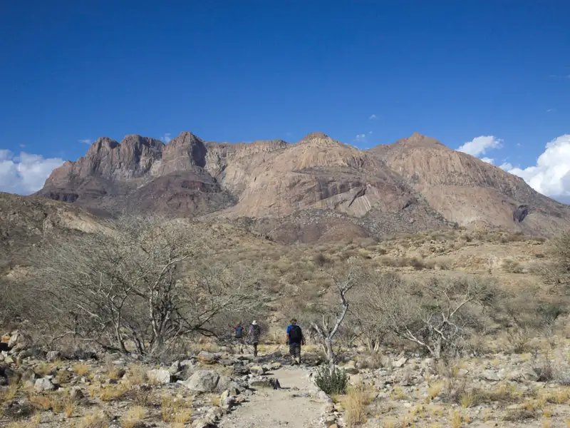 Wanderer auf einem Bergpfad in einer trockenen Landschaft.