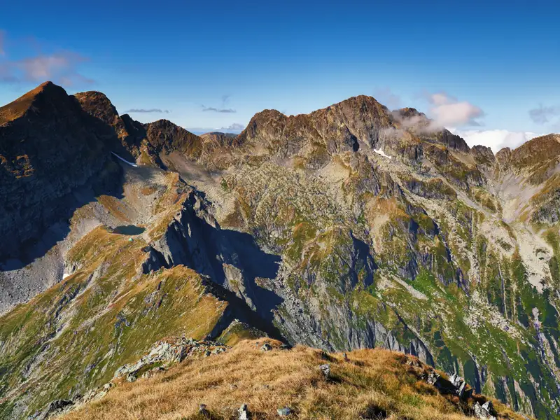 Felsige Berggipfel und grüne Täler unter blauem Himmel.
