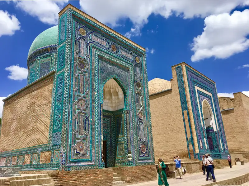 Türkisfarbene Mosaikfassade eines historischen Gebäudes mit kunstvollen Details und Besuchern.